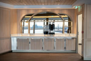 Modern galley kitchen with light wood cabinetry, arched mirrors, and integrated coffee station—designed for modular marine hospitality, offshore interiors, and cruise ship catering by ALMACO.