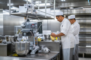 Commercial kitchen with chefs preparing dough beside an industrial mixer and stainless steel workstations—designed for modular marine catering, offshore galley systems, and hygienic food production by ALMACO.