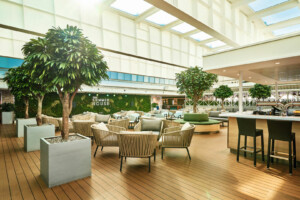 Spacious indoor lounge labeled 'Summer House' with natural lighting, modular seating, wooden flooring, and plant-integrated design—ideal for cruise ship lounges, offshore relaxation areas, and marine hospitality by ALMACO.
