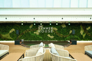 Indoor event space 'The Summer House' featuring a plant-covered stage backdrop, modular seating layout, and marine-grade hospitality design—ideal for cruise ships, offshore platforms, and luxury marine venues by ALMACO.