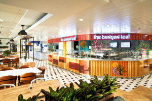 Vibrant food court restaurant 'The Banyan Leaf' with modular catering layout, decorative lighting, patterned flooring, and plant-integrated design—ideal for marine hospitality and offshore galley environments by ALMACO.