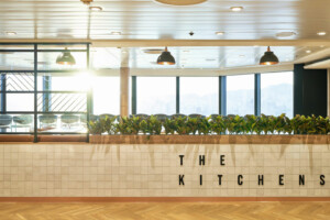 Modern galley interior labeled 'The Kitchens' with natural lighting, green plant decor, and hygienic modular design—ideal for marine, offshore, and hospitality catering environments by ALMACO.