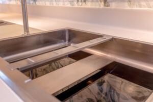 Modern double-basin stainless steel sink with decorative foliage backsplash, integrated into a white countertop for marine galley or offshore kitchen environments.