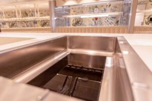 Stainless steel sink in a commercial galley kitchen with mirrored backsplash, decorative foliage design, and integrated food service equipment for marine and offshore use.