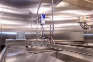 Heavy-duty stainless steel industrial sink with pre-rinse spray faucet, soap dispenser, and control box, designed for marine galley hygiene and offshore kitchen sanitation.