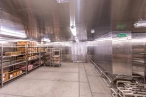 Industrial stainless steel walk-in refrigerator with mobile tray racks and shelving, designed for marine galley cold storage and offshore food preservation.