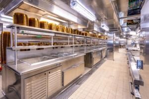 Industrial kitchen with stainless steel countertops and golden plate stacks – clean, organized space for high-volume food preparation in commercial or marine catering.