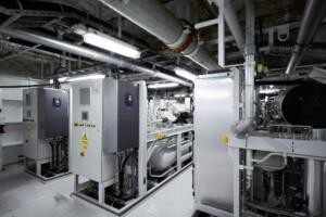 ALMACO industrial control room with dual-panel systems, overhead piping, and mechanical components. Engineered for marine and offshore applications with clean, efficient layout and advanced monitoring systems.
