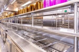 Commercial foodservice area with stainless steel counters and stacked golden and purple trays – ALMACO marine catering logistics and galley equipment