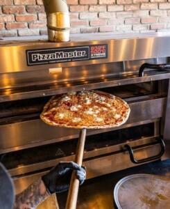 Pizza being removed from PizzaMaster oven with 932°F display using a pizza peel – ALMACO marine galley and foodservice equipment