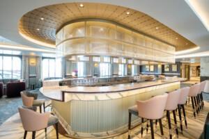 Modern marine bar area with curved marble counter, pink upholstered chairs, and golden lattice lighting – ALMACO modular hospitality and lounge design