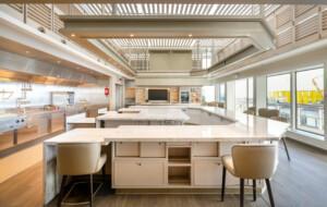 Spacious modern galley kitchen with central island, stainless steel appliances, and bar seating – ALMACO marine hospitality and modular foodservice design