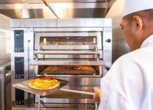 Chef using pizza peel to operate industrial pizza oven with dual compartments – ALMACO marine galley equipment and foodservice solutions