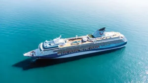 Marella Discovery cruise ship docked at a scenic port with lush green hills in the background and a cloudy sky above, representing ALMACO’s turnkey marine accommodation and modular outfitting solutions.
