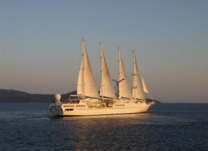 Four-masted white sailing ship cruising on calm waters during sunrise or sunset, with distant hills in the background, representing ALMACO’s turnkey marine outfitting and modular accommodation solutions for classic and hybrid vessels.